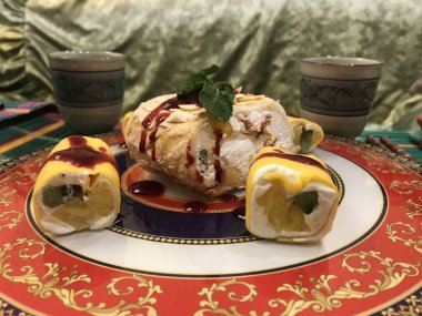 Asya fincanlarının ve yeşil kumaşların arka planında meyveli ruloların yanında parlak bir Asya tabağında güzel bir krema rulosu..