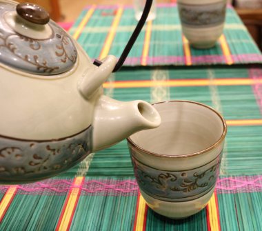 Asyalı bir çaydanlığın ağzı Asya Kupası 'nın üzerine eğilir parlak bir Asyalı mindere karşı.