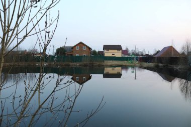 Akşam gökyüzünün arka planındaki eski yazlık evler söğüt ağacının yetiştiği göle yansıyor. Fotoğraf doğal akşam ışığında çekildi..