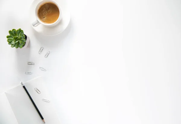 Üst kattaki ofis masasında yatıyordu. Çalışma alanı boş pano, ofis malzemeleri, kalem, yeşil yaprak ve beyaz arka planda kahve fincanı. Boşluğu kopyala.