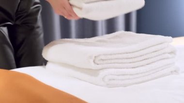 Kadın elleri temiz beyaz banyo havlularını yatağın üzerine koyuyor. Temizlik servisi.  