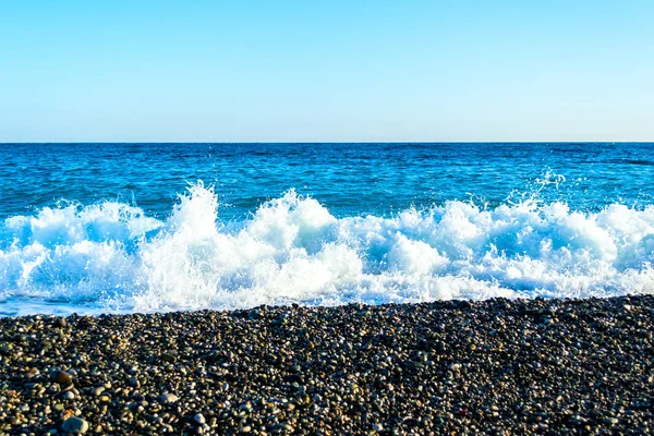 Wellen brechen an einem steinigen Strand auf und bilden Gischt — Stockfoto