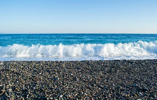 Wellen brechen an einem steinigen Strand auf und bilden Gischt — Stockfoto