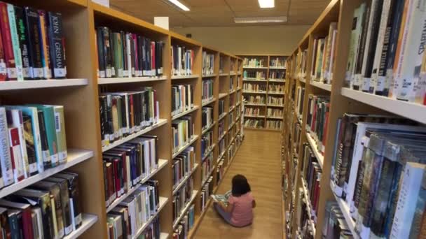 Ung flicka läser en serietidning som sitter på golvet i ett bibliotek — Stockvideo