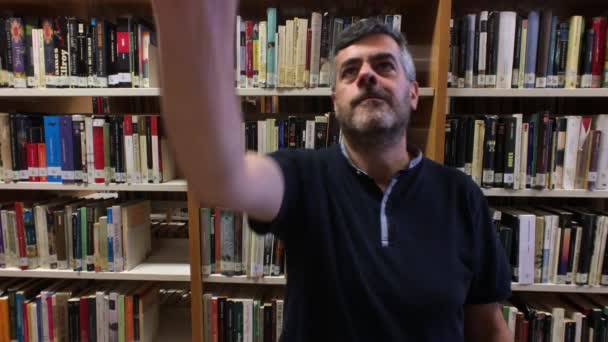 Medelålders man ser ut och plocka upp en bok i ett bibliotek — Stockvideo