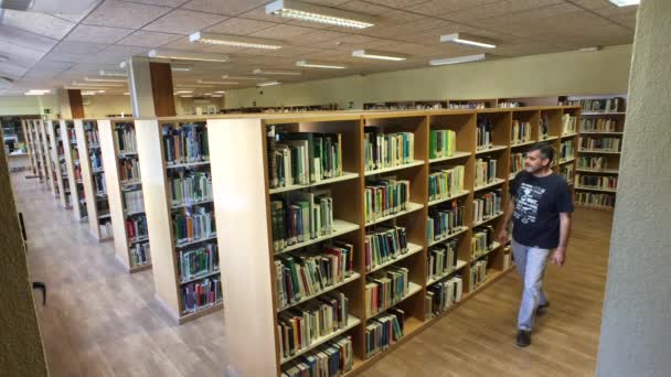 Medelålders man ser ut och plocka upp en bok i ett bibliotek — Stockvideo