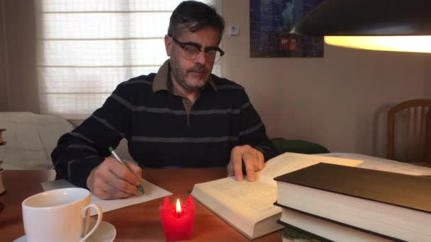 Hombre de mediana edad toma notas de un libro sentado en su casa — Vídeo de stock