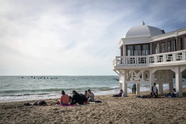 Playa de Caleta en el centro de la ciudad vieja es la más popular de las playas, Grupo de jóvenes disfrutando de una tarde soleada sentado en la arena, tomar en Cádiz, Andalucía, España — Foto de Stock