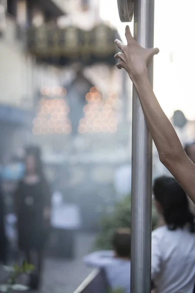 Joven agarra fuertemente con su brazo un poste de luz durante Semana Santa, imagen conceptual, en el fondo una mujer vestida de manto junto a la llamada en español "Palio" de la figura de María Esperanza, toma en Linares, España — Foto de Stock