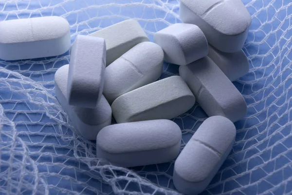 Algumas pílulas brancas embrulhadas em gaze em um fundo azul — Fotografia de Stock