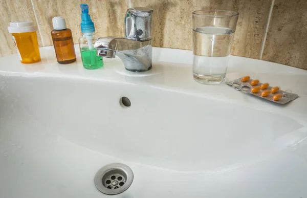 Lavabo avec plusieurs bouteilles de médicaments et un verre d'eau — Photo