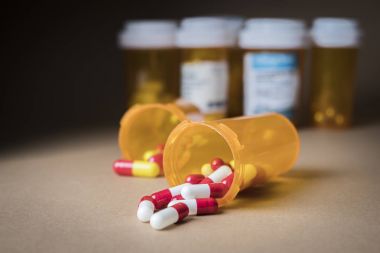 Açık bir şişe kahverengi zemin üzerine dökülüp beyaz ve kırmızı hap