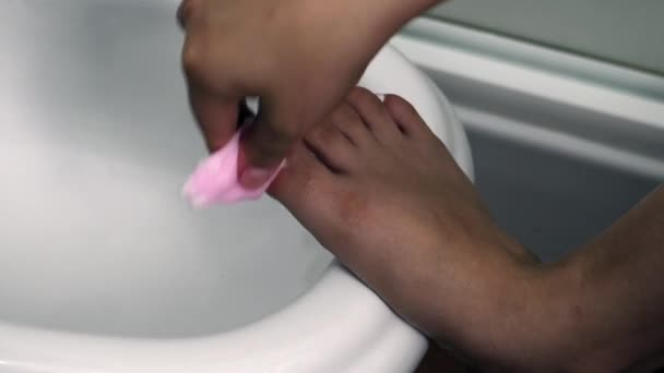 Una adolescente envejecida quita el esmalte de uñas con un algodón en el baño — Vídeos de Stock