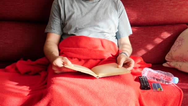 Больной человек читает в кресле своего дома принять таблетку и соединяет телевизор с контролем на расстоянии — стоковое видео