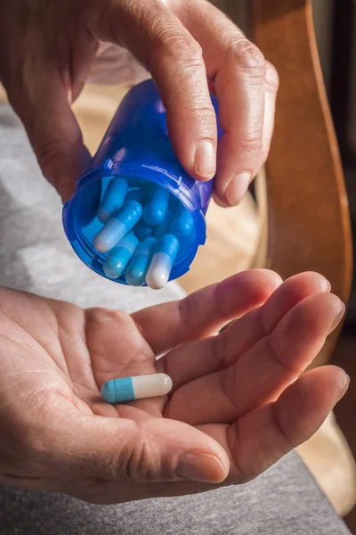 Женщины берут белую и синюю капсулу правой рукой из голубой прозрачной бутылки — стоковое фото