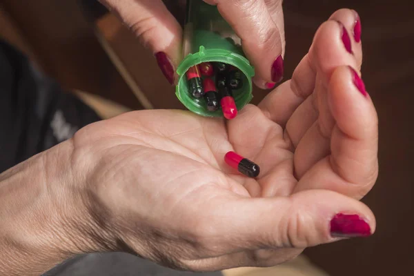 Vrouwen nemen rode en zwarte capsule met rechterhand van een groene fles op zwarte achtergrond — Stockfoto