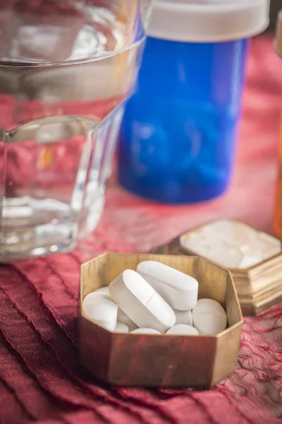 Picaporte metálico con pastillas blancas junto con vidrio de agua —  Fotos de Stock