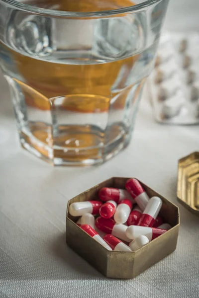 Casemate métallique avec capsules blanches et rouges avec verre d'eau — Photo