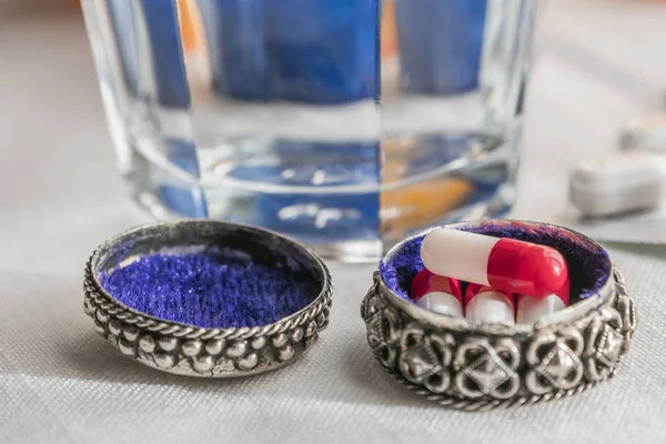 Metalen pillendoos met witte en rode capsules samen met waterglas — Stockfoto