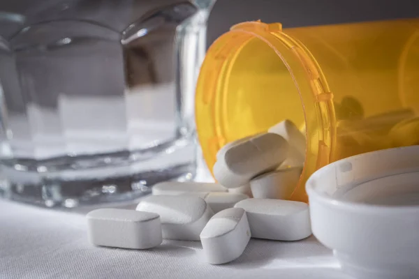 Some pills of different size and color along with a water glass — Stock Photo, Image