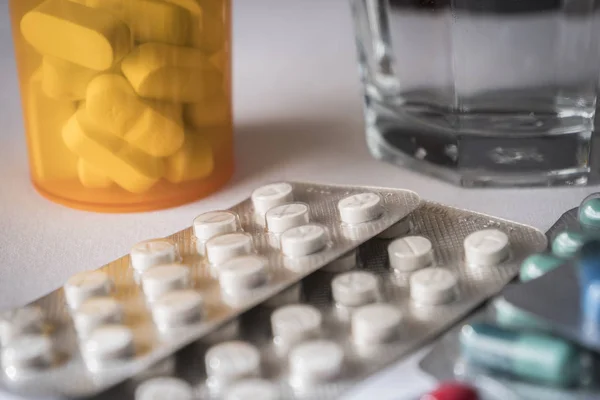 Algunas pastillas de diferente tamaño y color junto con un vaso de agua —  Fotos de Stock