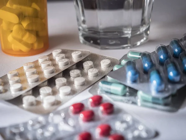 Algunas pastillas de diferente tamaño y color junto con un vaso de agua — Foto de Stock