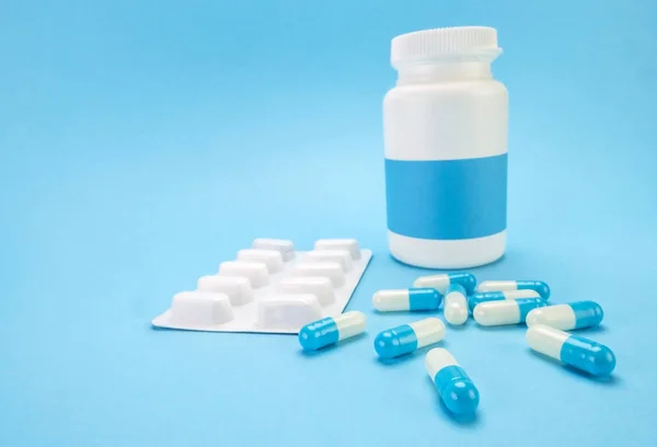 Pills spilling from an open bottle on blue background — Stock Photo, Image