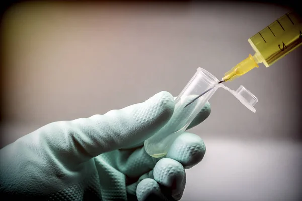 Cientista com luvas de látex verde manipula frasco e seringa em laboratório, imagem conceitual — Fotografia de Stock