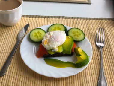 Beyaz tabakta kahve, siyah ekmek ve avokado ile haşlanmış yumurta.