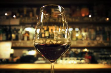 Bir bardak kırmızı şarap, arka planda bulanık alkol şişeleriyle içmek (sıcak ton))