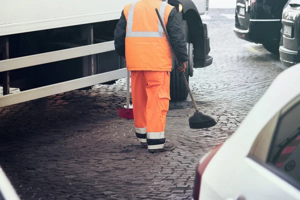 worker pick up the trash on the street, man working with cleaning tools on the road near the cars