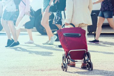 Jet üzerinde tramvayı olan bir adam, kentsel bir yerde bavulla yürüyor (arka planda odaklanmış bir grup insan)
