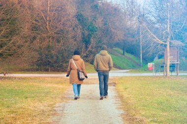 Yürüyen genç bir çiftin arka görüntüsü. Parkta genç bir kadın ve bir adam anayasal açıdan sessiz kalıyor.
