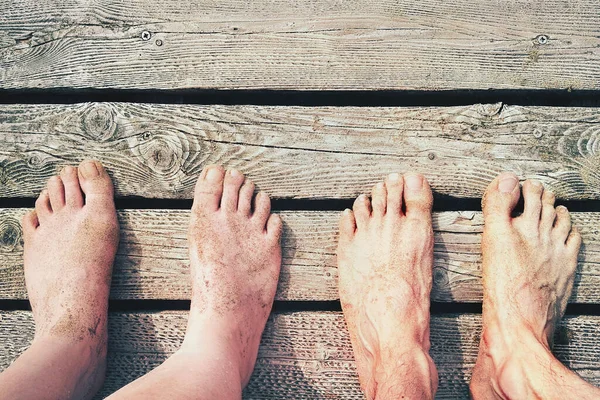 Top View Of Couple Feet In Vacation. Two lovers (boy and girl) standing on outdoor wooden floor. The feet are dirty of sand