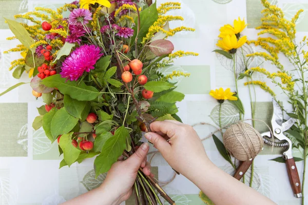 Florist hands making bouquet with fall flowers and berries