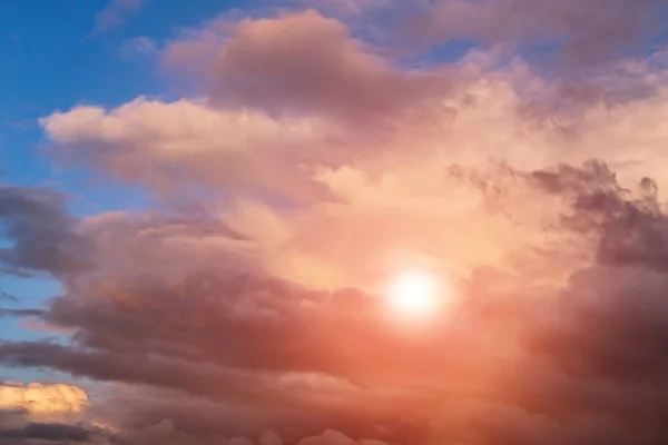 Dramatic sunset storm sky with cumulus clouds, orange sun and sunlight on blue sky background