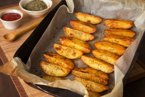Container with homemade baked potato wedges with spices on parchment paper