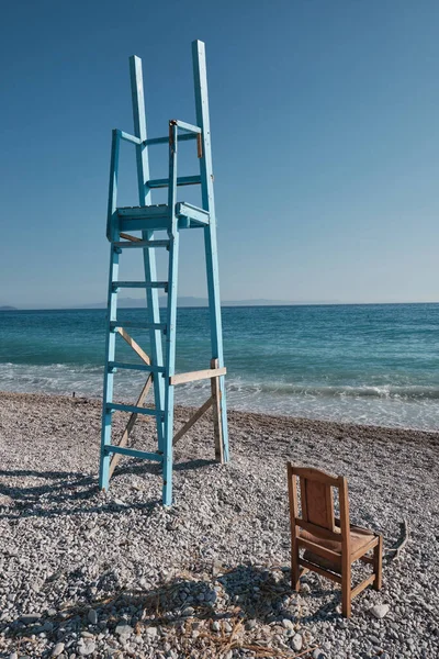 Mavi cankurtaran koltuğu kulesi ve sandalye Arnavutluk 'ta bir plajda, uzaktaki korfu adasıyla birlikte.