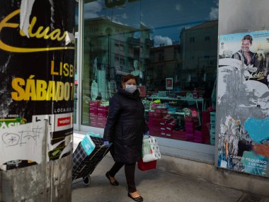 Elinde tuvalet kağıdıyla sokakta yürüyen maskeli bir kadın. Portekiz 'de karantina