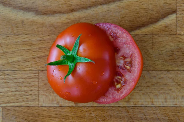 Mükemmel sulu taze kırmızı domates bir tahta üzerinde Su damlacıkları bir kesim içinde yeşil yaprakları ile