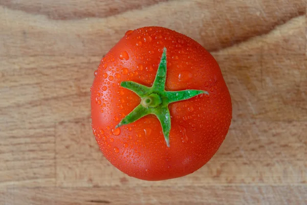 Tomate vermelho fresco suculento perfeito com folhas verdes em gotas de água em uma placa de corte — Fotografia de Stock