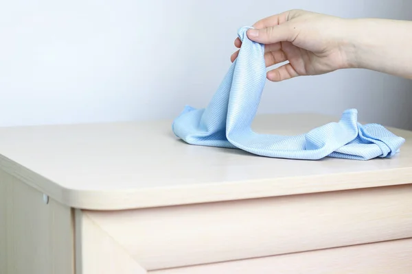 Een vrouwelijke hand houdt een microvezel doek over een ladekast. Kopieer ruimte - het concept van huisreiniging, reinheid, de vernietiging van bacteriën. — Stockfoto
