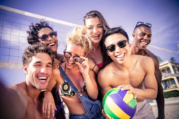 Счастливые друзья играют в пляжный волейбол — стоковое фото
