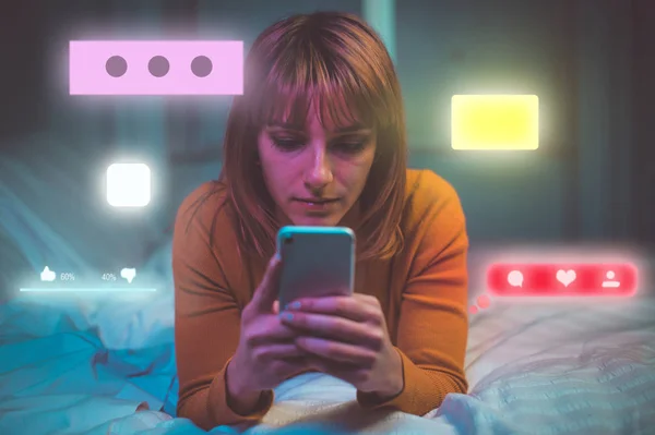 Fiatal nő sms-ezik a telefonon, miközben fekszik az ágyban — Stock Fotó