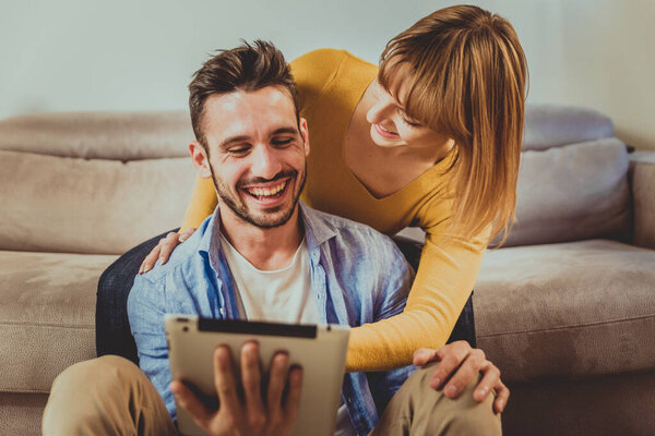 Two young adults at home - Beautiful couple using computer tablet at home to shop online