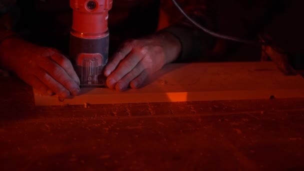 Blanke man snijdt een figuur met een decoupeerzaag in toekomstige houten meubels met rood licht — Stockvideo