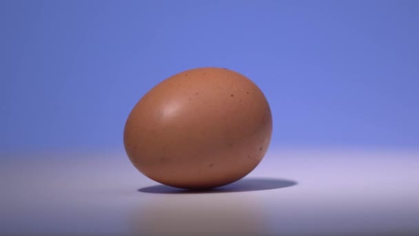 Το αυγό περιστρέφεται στη λευκή επιφάνεια με φόντο μπλε βαθμίδας. 4K κοντινό πλάνο — Αρχείο Βίντεο