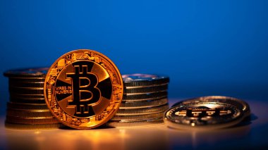 Ön planda altın Bitcoin ve arka planda mavi ışıklı bir sürü gümüş sikke. Masadaki yansıma