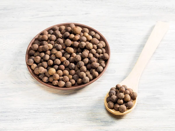 Allspice i lera platta och trä sked på en vit bakgrund. Jag — Stockfoto