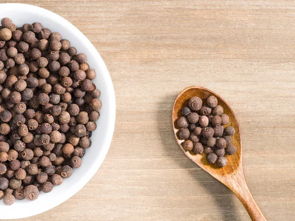 Allspice in witte schaal en lepel op een bruine houten ondergrond. I — Stockfoto